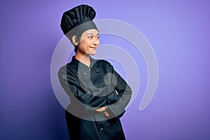 Young beautiful chinese chef woman wearing cooker uniform and hat over purple background looking to the side with arms crossed