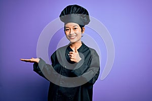 Young beautiful chinese chef woman wearing cooker uniform and hat over purple background Showing palm hand and doing ok gesture
