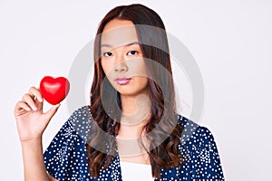 Young beautiful chinese girl holding heart thinking attitude and sober expression looking self confident
