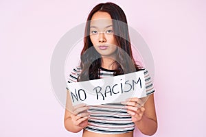 Young beautiful chinese girl holding no racism banner thinking attitude and sober expression looking self confident