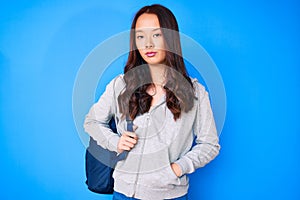 Young beautiful chinese girl holding student backpack thinking attitude and sober expression looking self confident