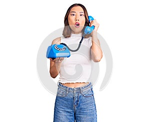 Young beautiful chinese girl holding vintage telephone scared and amazed with open mouth for surprise, disbelief face