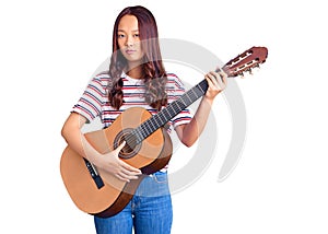 Young beautiful chinese girl playing classical guitar thinking attitude and sober expression looking self confident