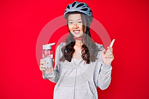 Young beautiful chinese girl wearing bike helmet and holding water bottle smiling happy pointing with hand and finger to the side