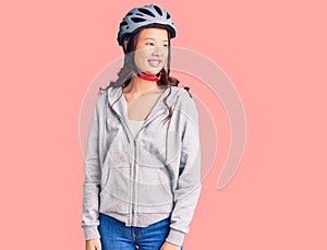 Young beautiful chinese girl wearing bike helmet looking away to side with smile on face, natural expression