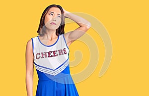 Young beautiful chinese girl wearing cheerleader uniform confuse and wondering about question
