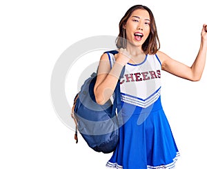 Young beautiful chinese girl wearing cheerleader uniform holding student backpack screaming proud, celebrating victory and success