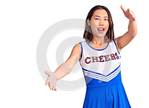 Young beautiful chinese girl wearing cheerleader uniform looking at the camera smiling with open arms for hug