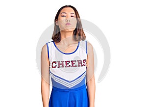 Young beautiful chinese girl wearing cheerleader uniform puffing cheeks with funny face