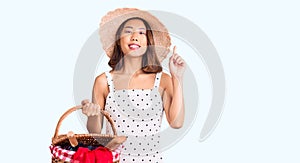 Young beautiful chinese girl wearing summer hat holding picnic basket surprised with an idea or question pointing finger with