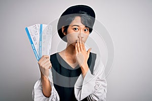 Young beautiful chinese tourist woman holding boarding pass airlane over white background cover mouth with hand shocked with shame