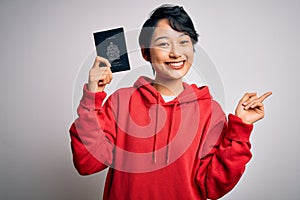 Young beautiful chinese tourist woman on vacation holding canada canadian passport very happy pointing with hand and finger to the