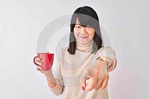 Young beautiful Chinese woman drinking red cup of coffee over isolated white background pointing with finger to the camera and to