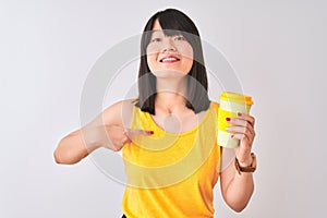 Young beautiful Chinese woman drinking take away coffee over isolated white background with surprise face pointing finger to