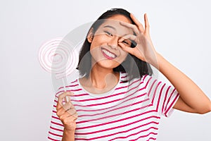 Young beautiful chinese woman eating lollipop standing over isolated white background with happy face smiling doing ok sign with