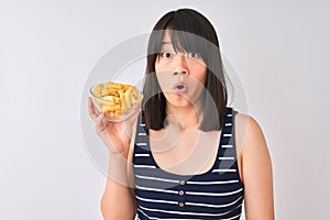 Young beautiful Chinese woman holding bowl with macaroni over isolated white background scared in shock with a surprise face,