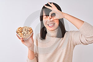 Young beautiful Chinese woman holding bowl with peanuts over isolated white background with happy face smiling doing ok sign with