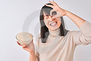 Young beautiful Chinese woman holding bowl with rice over isolated white background with happy face smiling doing ok sign with