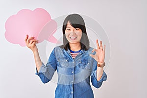 Young beautiful Chinese woman holding cloud speech bubble over isolated white background doing ok sign with fingers, excellent