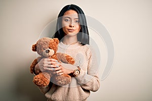 Young beautiful chinese woman holding teddy bear standing over isolated white background with a confident expression on smart face