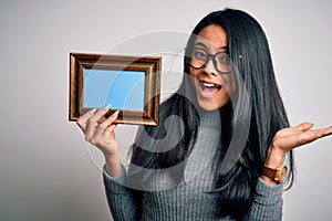 Young beautiful chinese woman holding vintage frame over isolated white background very happy and excited, winner expression