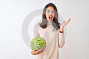 Young beautiful chinese woman holding watermelon standing over isolated white background very happy and excited, winner expression