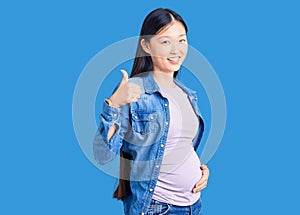 Young beautiful chinese woman pregnant expecting baby doing happy thumbs up gesture with hand