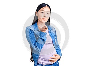Young beautiful chinese woman pregnant expecting baby looking at the camera blowing a kiss with hand on air being lovely and sexy
