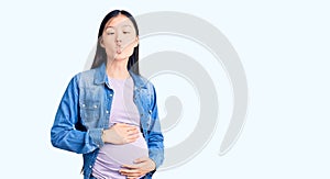 Young beautiful chinese woman pregnant expecting baby making fish face with lips, crazy and comical gesture