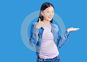 Young beautiful chinese woman pregnant expecting baby showing palm hand and doing ok gesture with thumbs up, smiling happy and