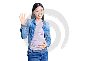 Young beautiful chinese woman pregnant expecting baby showing and pointing up with fingers number five while smiling confident and