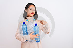 Young beautiful chinese woman recycling plastic bottles over isolated white background with surprise face pointing finger to