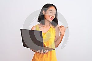 Young beautiful chinese woman using laptop standing over isolated white background pointing and showing with thumb up to the side