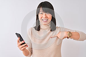 Young beautiful Chinese woman using smartphone standing over isolated white background with surprise face pointing finger to