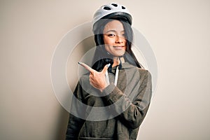 Young beautiful chinese woman wearing bike helmet over isolated white background cheerful with a smile of face pointing with hand