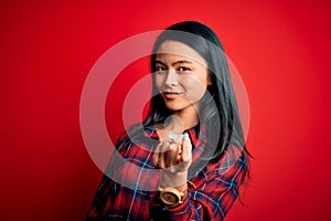 Young beautiful chinese woman wearing casual shirt over isolated red background Beckoning come here gesture with hand inviting