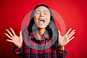 Young beautiful chinese woman wearing casual shirt over isolated red background celebrating mad and crazy for success with arms