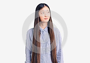 Young beautiful chinese woman wearing casual shirt smiling looking to the side and staring away thinking