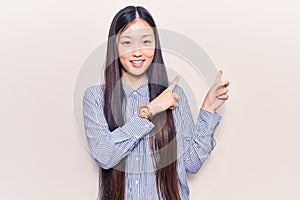 Young beautiful chinese woman wearing casual striped shirt smiling and looking at the camera pointing with two hands and fingers