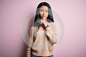 Young beautiful chinese woman wearing casual sweater over isolated pink background asking to be quiet with finger on lips