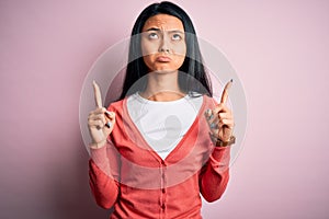 Young beautiful chinese woman wearing casual sweater over isolated pink background Pointing up looking sad and upset, indicating