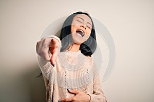 Young beautiful chinese woman wearing casual sweater over isolated white background laughing at you, pointing finger to the camera