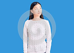 Young beautiful chinese woman wearing casual sweater smiling looking to the side and staring away thinking