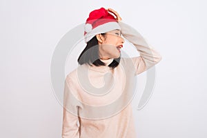 Young beautiful chinese woman wearing Christmas Santa hat over isolated white background surprised with hand on head for mistake,