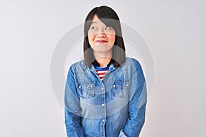 Young beautiful chinese woman wearing denim shirt over isolated white background smiling looking to the side and staring away