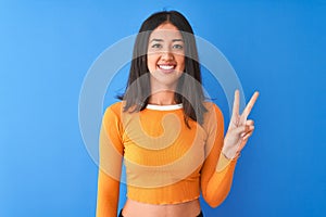 Young beautiful chinese woman wearing orange t-shirt standing over isolated blue background showing and pointing up with fingers