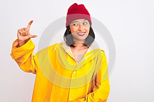 Young beautiful chinese woman wearing raincoat and wool cap over isolated white background smiling and confident gesturing with