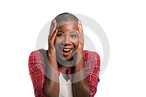 Young beautiful and cool black African American woman in casual shirt and shaved hair excited and surprised isolated on dark