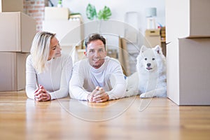 Young beautiful couple with dog lying down on the floor at new home around cardboard boxes