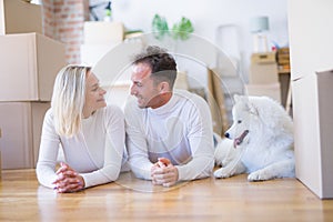 Young beautiful couple with dog lying down on the floor at new home around cardboard boxes